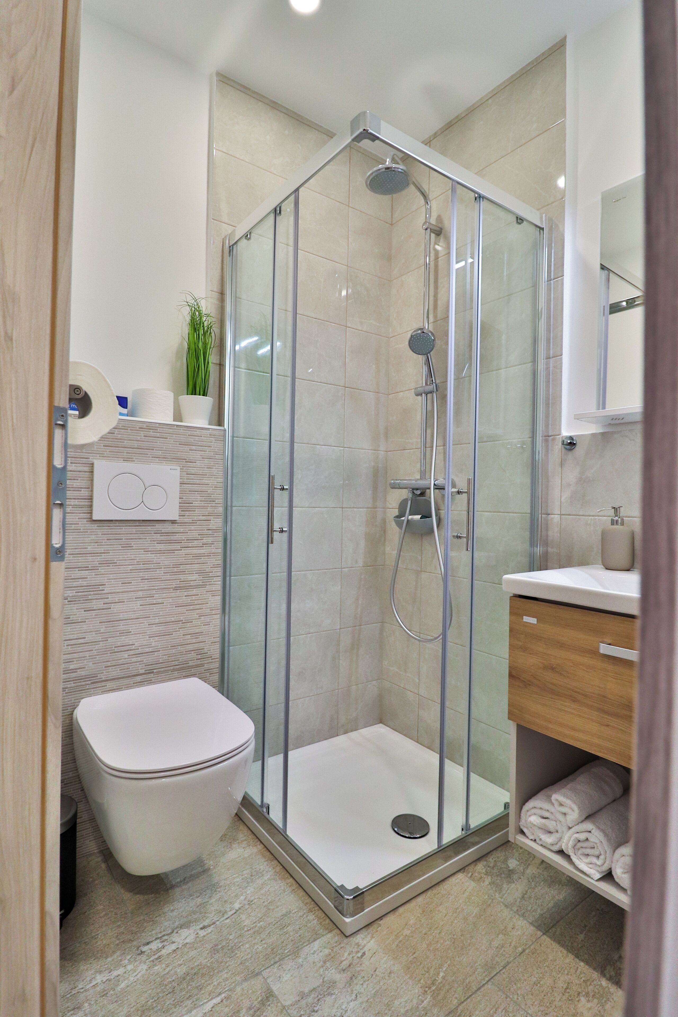 A modern bathroom with a glass-enclosed shower, a toilet, a sink with a wooden cabinet, and a towel rack.