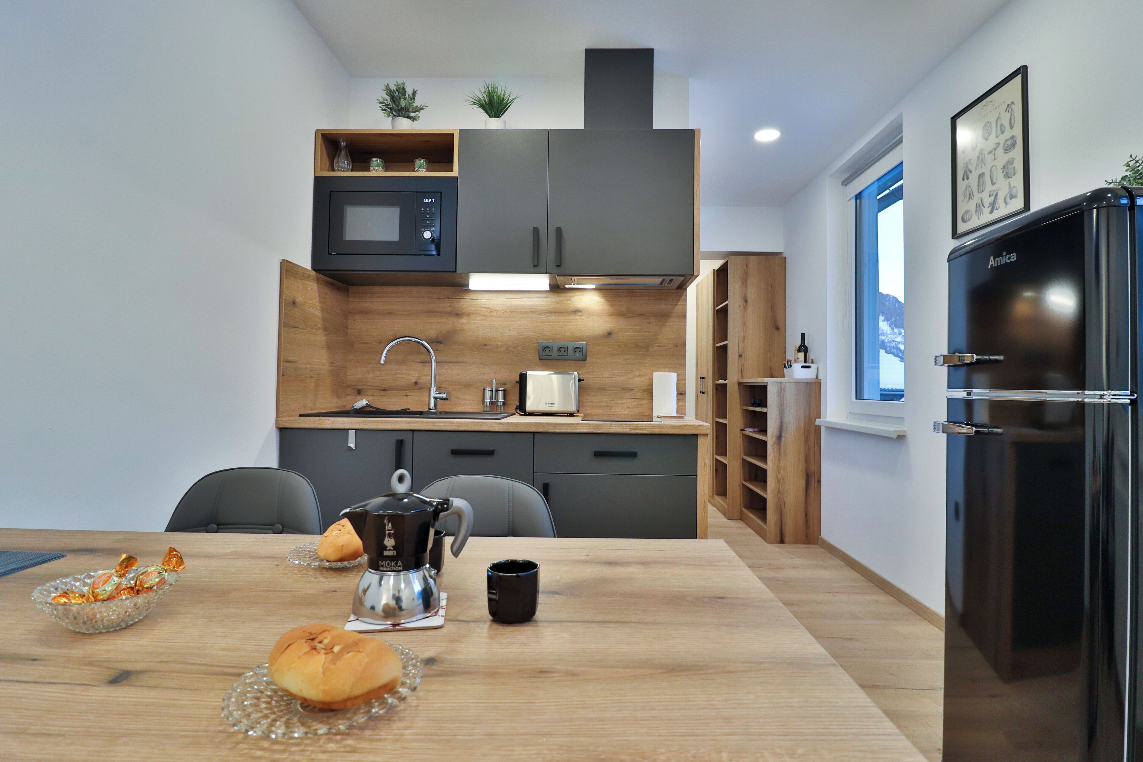 Une cuisine moderne avec une table en bois, une machine à café et un réfrigérateur noir.