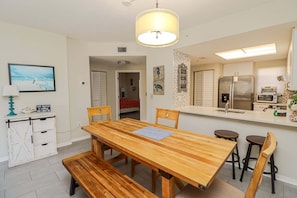 A dining area with a wooden table, benches, and a kitchen with appliances. - Ocean Village Club Condo Q26 (St. Augustine)
