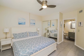 A bedroom with a bed, nightstands, a ceiling fan, and a bathroom visible through an open door. - Ocean Village Club Condo Q26 (St. Augustine)
