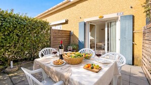 An outdoor dining area with a table set for two, a bottle of wine, and a basket of bread and fruit. - L’Instant Douceur, 2 guests, Pool in Calvisson (Calvisson)