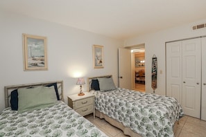 A bedroom with two beds, a nightstand, a lamp, and a door leading to another room. - SABTC 113-Ground Floor Two Bedroom Condo in Oceanfront Building (St. Augustine)