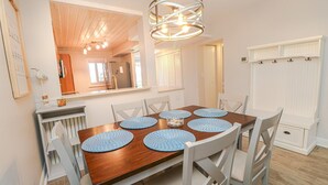 Uma sala de jantar com mesa de madeira, cadeiras brancas e jogos americanos azuis.