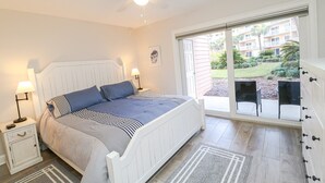 Quarto com cama, mesas de cabeceira, ventoinha no teto e vista para um pátio exterior com cadeiras.