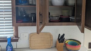 A kitchen with wooden cabinets, a cutting board, a sink, and various kitchen utensils. - Spacious Frederick County Retreat (Middletown)