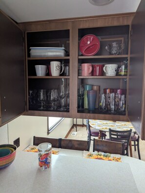 A kitchen with wooden cabinets, a dining table with chairs, and various kitchenware including cups, glasses, and a canister. - Spacious Frederick County Retreat (Middletown)