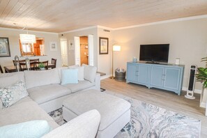 A modern living room with a sectional sofa, a TV, a cabinet, and a floor lamp. - SABTC 214-Beautiful, Updated 3 Bedroom Condo With Pool View! (St. Augustine)
