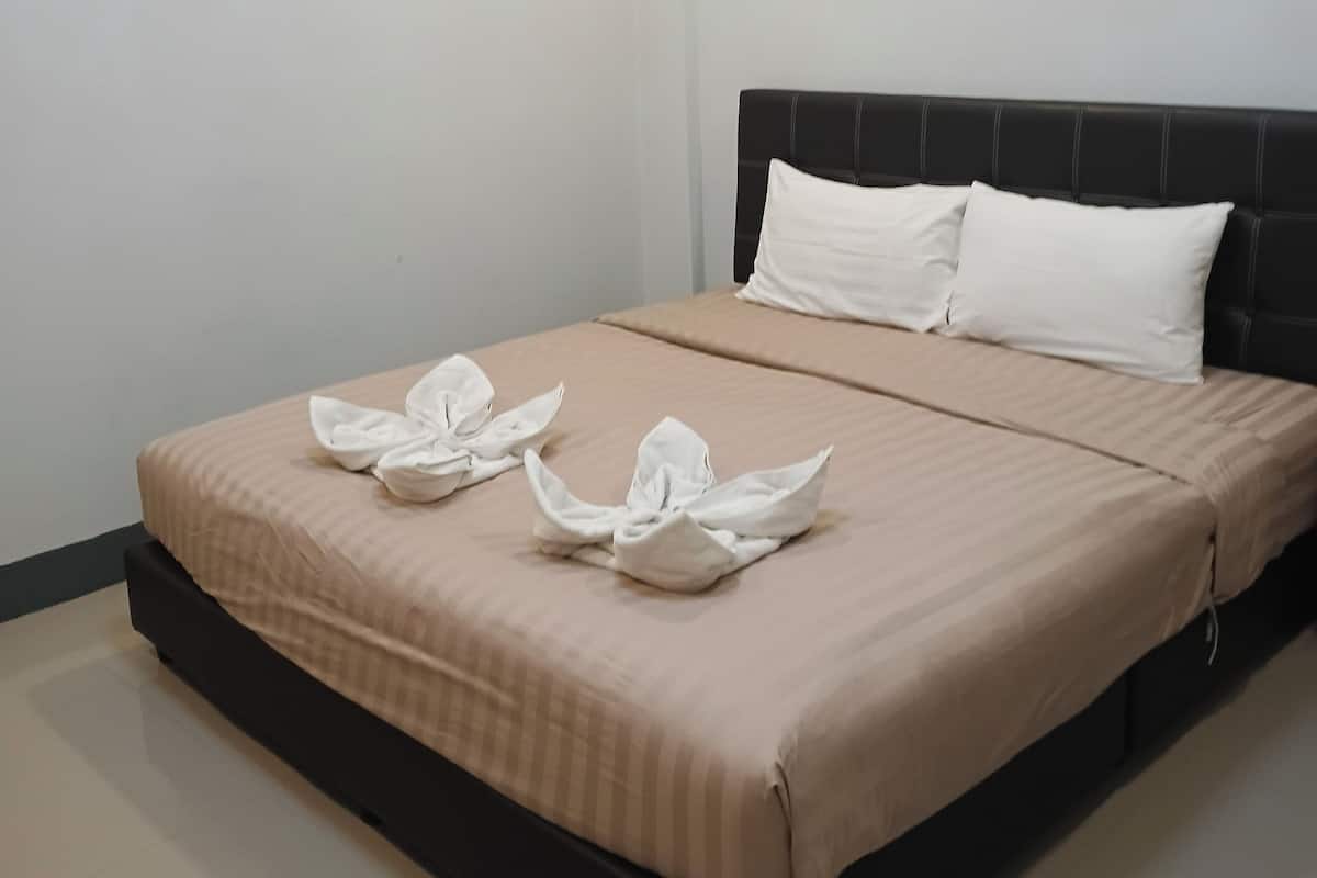 A neatly made bed with a headboard, a plain wall, and a ceiling light.