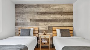 A bedroom with two beds, a wooden headboard, a small bedside table with a lamp, and a basket of towels. - 426 Hotel du Lac (Mont-Tremblant)