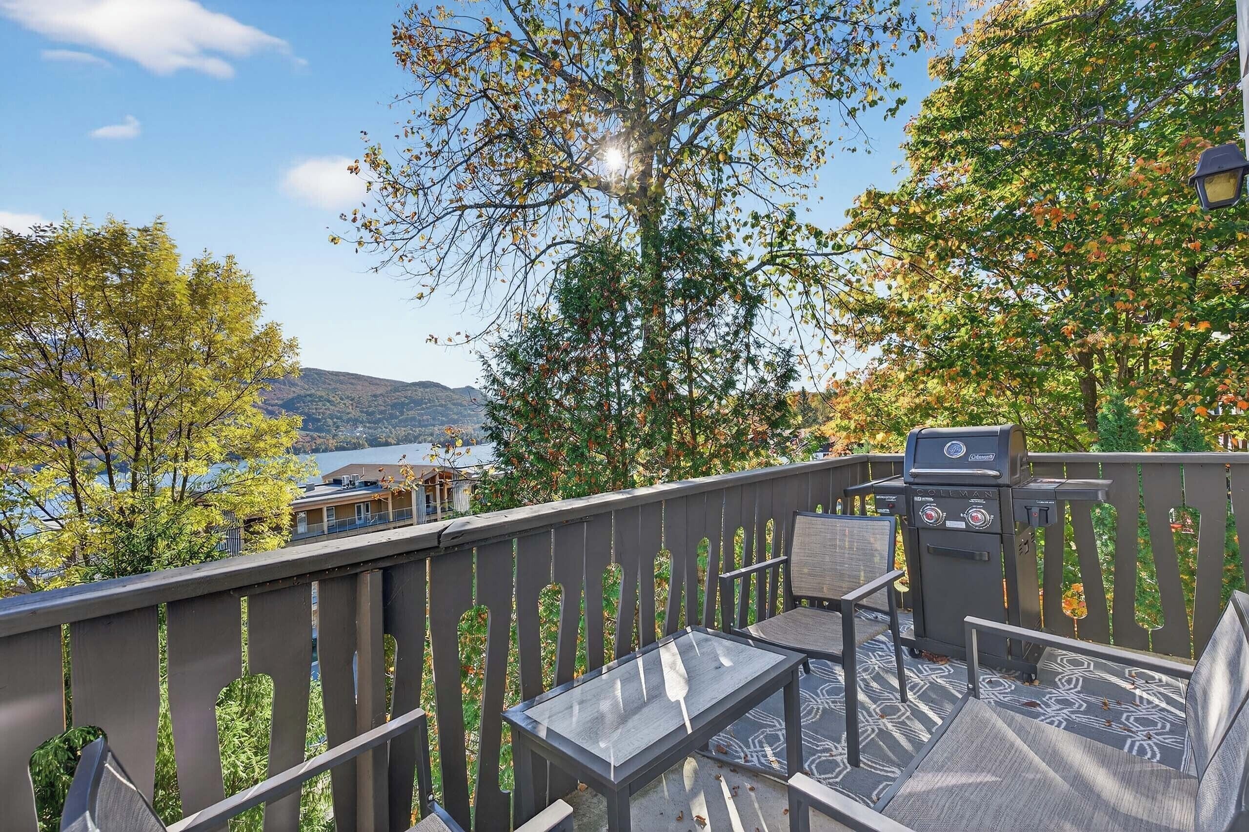 Ein Balkon mit Grill, Sitzgelegenheit und Blick auf See und Berge.