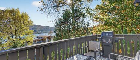 Ein Balkon mit Grill, Sitzgelegenheit und Blick auf See und Berge.