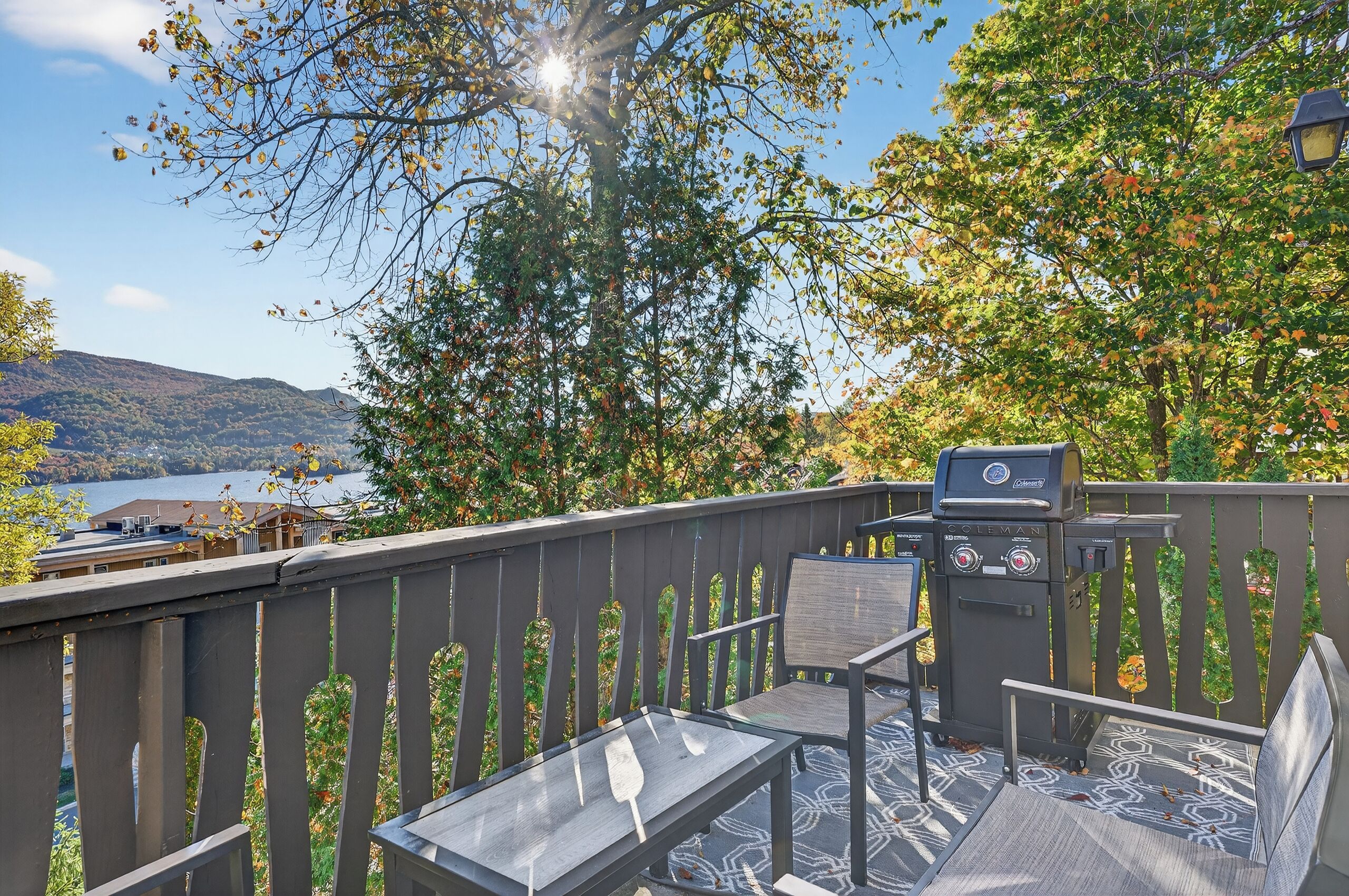 A patio with a grill, seating, and a view of a lake and hills.