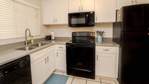 Una cocina compacta con armarios blancos, una estufa negra, un microondas negro y un refrigerador negro.