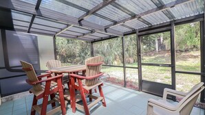 Un patio cubierto con mesa y sillas, ventanas amplias y vista a follaje.