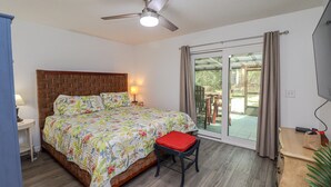 Un dormitorio con cama, mesita de noche, escritorio, silla, ventilador de techo y puerta corrediza de vidrio que da a un área exterior.