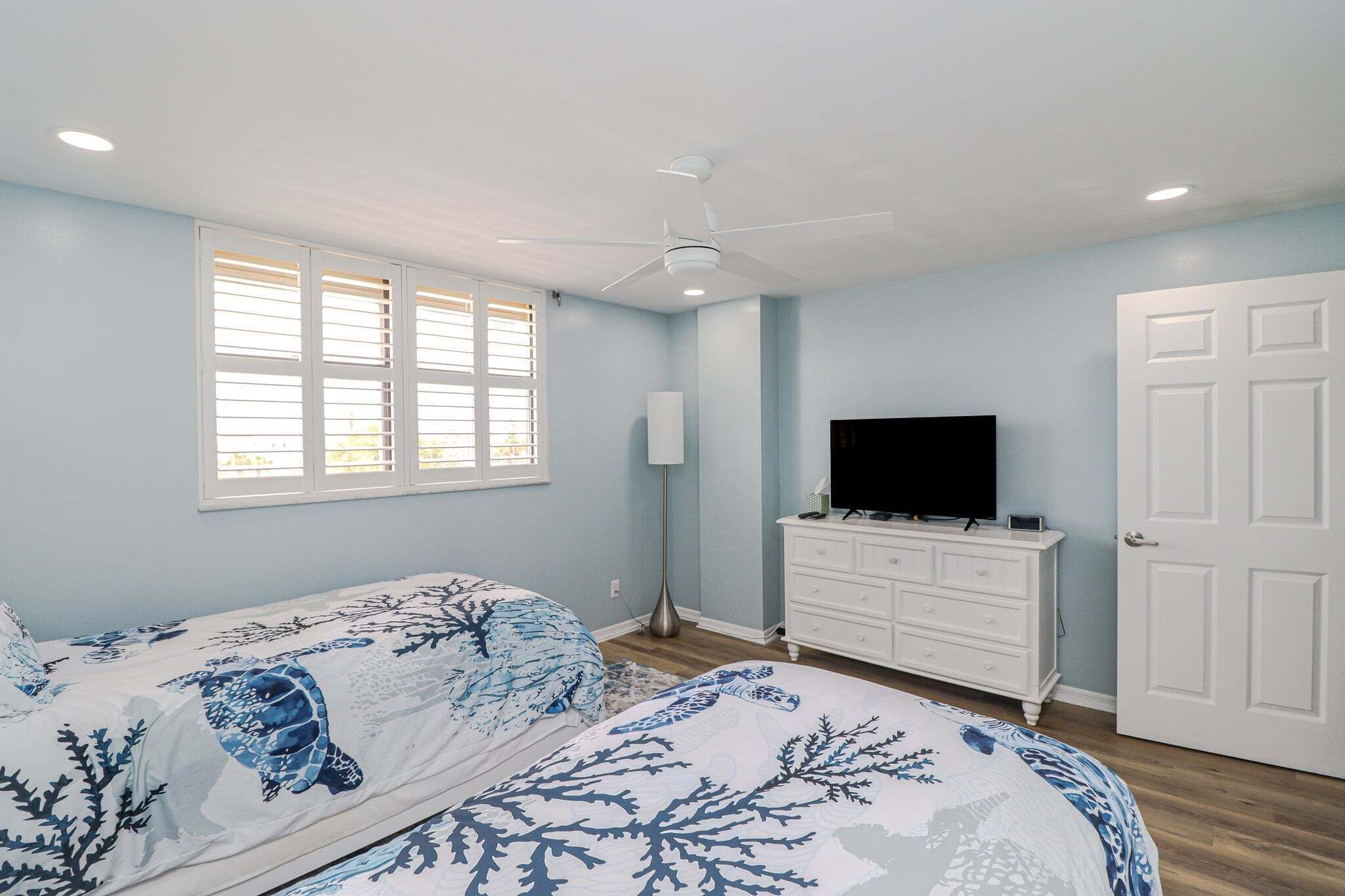 A bedroom with two beds, a ceiling fan, a TV, a dresser, and a door.
