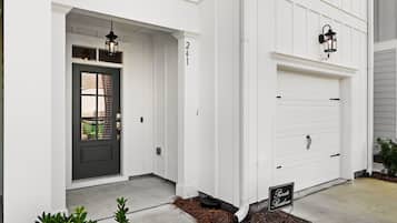 Une maison blanche avec une porte d’entrée sombre, une porte de garage et une boîte aux lettres.