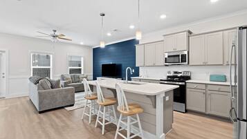 A modern kitchen with a central island, bar stools, a microwave, stove, and a refrigerator.