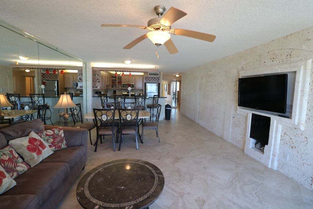 A spacious living room with a ceiling fan, a dining area, and a kitchen in the background.