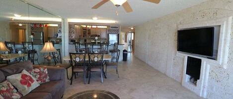 A spacious living room with a ceiling fan, a dining area, and a kitchen in the background.