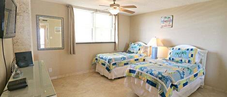 A hotel room with two beds, a ceiling fan, a large mirror, and a desk with a computer.