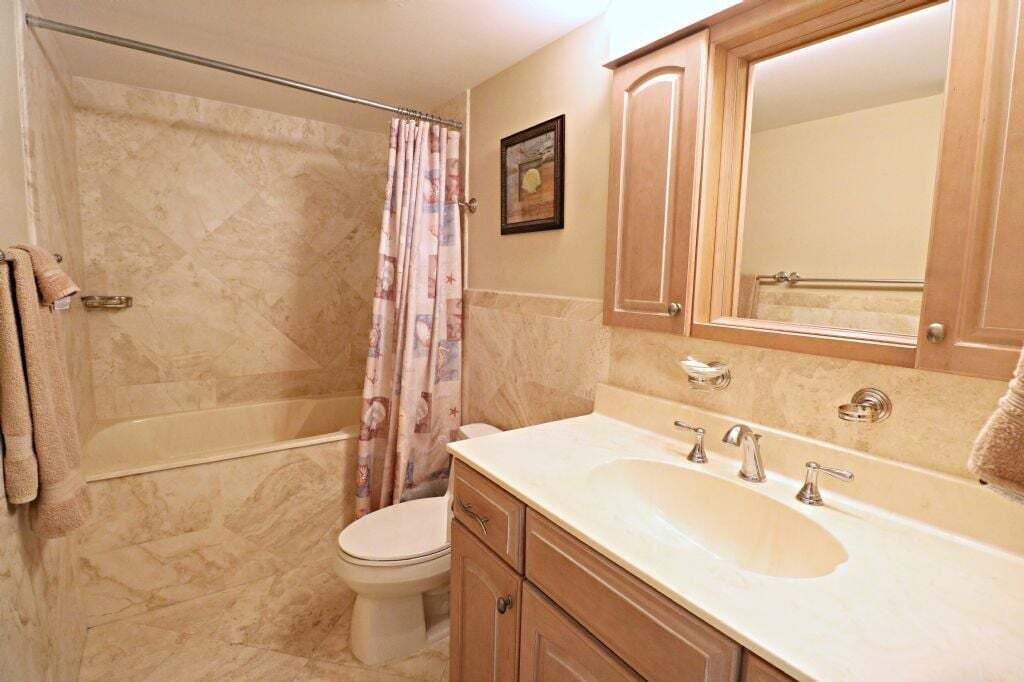 Un bany amb banyera, vàter i un lavabo amb un mirall a sobre.