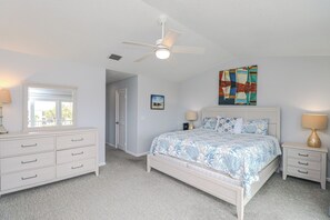 Ein Schlafzimmer mit Bett, Nachttisch, Kommode, Deckenventilator, Fenster und Tür.