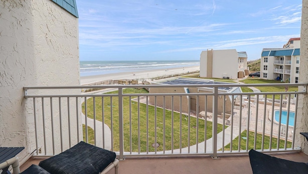 Ein Balkon mit Blick auf den Strand, ein Schwimmbad und ein Gebäude mit blauem Dach.