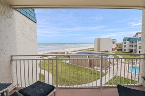A balcony with a view of the beach, a swimming pool, and a building with a blue roof. - Pool, Beach Boardwalk, Boat Ramp & Fishing Pier! Trade Winds 53 (St. Augustine)