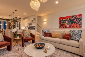 A modern living room with a sofa, armchairs, and a coffee table. There is a kitchen in the background with a dining area. - 2 Music City Homes | 20 Beds | Firepit & Hot Tub (Nashville)