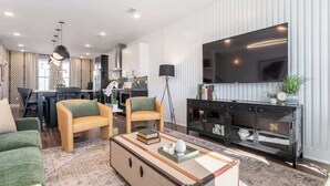 A modern living room with a sofa, armchairs, a coffee table, and a TV. - 2 Music City Homes | 20 Beds | Firepit & Hot Tub (Nashville)