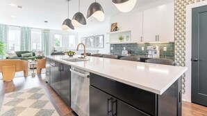 A modern kitchen with a central island, pendant lighting, and a view into the living area. - 2 Music City Homes | 20 Beds | Firepit & Hot Tub (Nashville)