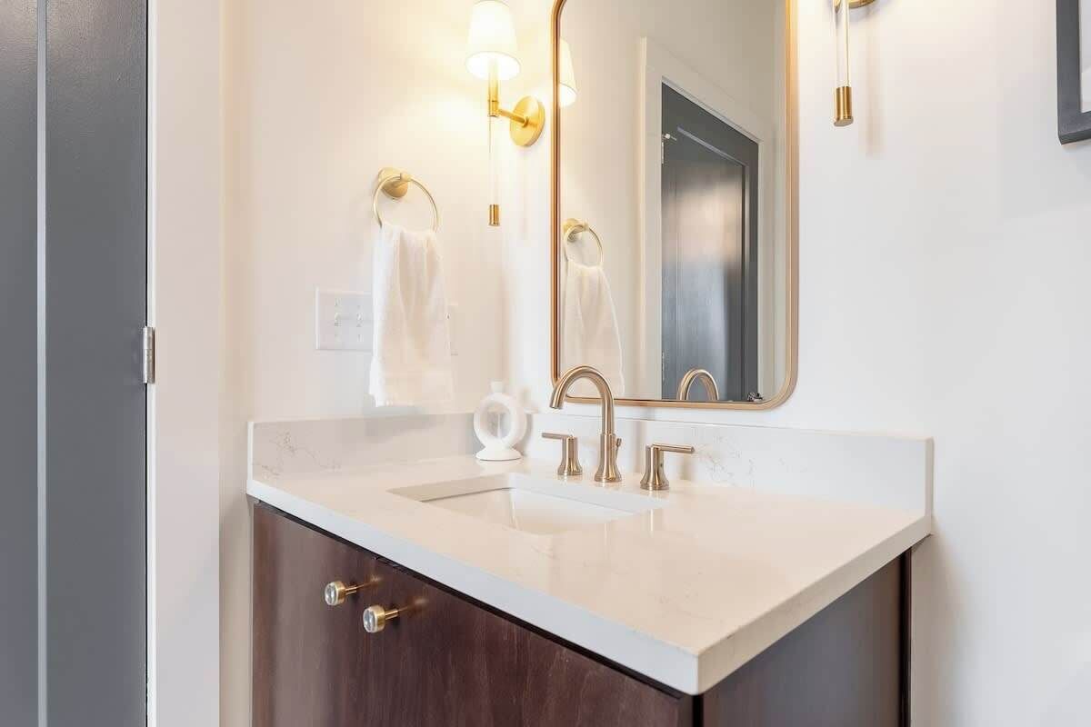 Une salle de bain avec un comptoir blanc, deux lavabos, un grand miroir et des accessoires dorés.