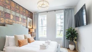 Ein modernes Hotelzimmer mit einem großen Bett, einer Kristallleuchtre, einem Flachbildfernseher und Blick auf die Stadt durch große Fenster.