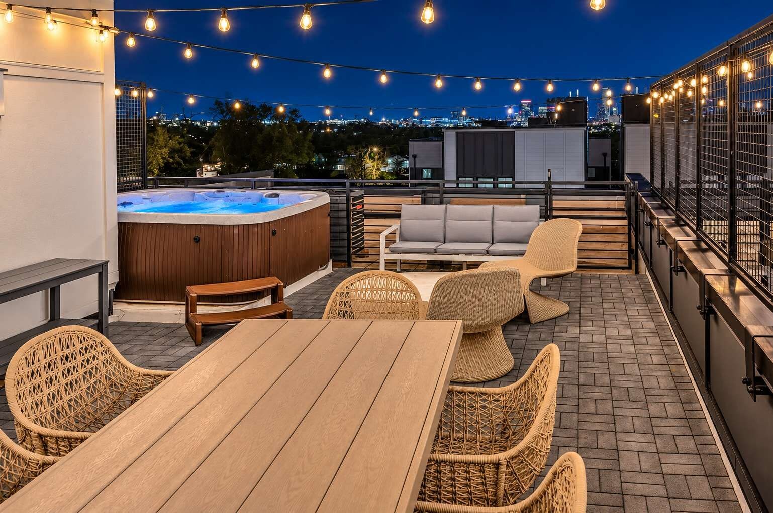 Eine Dachterrasse mit Whirlpool, Korbmöbeln und Lichterketten.