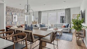 A modern living room with a dining area, featuring a large wooden table, comfortable seating, and a decorative wall. - 2 Chic Nashville Homes | Rooftops & Skyline Views (Nashville)