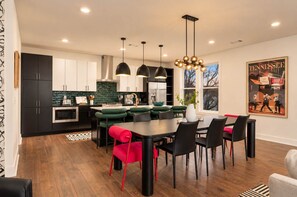 A modern kitchen with dark cabinets, a green backsplash, and a dining area with a black table and red chairs. - 2 Chic Nashville Homes | Rooftops & Skyline Views (Nashville)