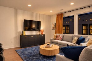 A modern living room with a flat-screen TV, a dark wood console, a round coffee table, and a sofa with patterned cushions. - 2 Chic Nashville Homes | Rooftops & Skyline Views (Nashville)