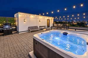 An outdoor patio with a hot tub, a grill, seating, and string lights. - 2 Chic Nashville Homes | Rooftops & Skyline Views (Nashville)