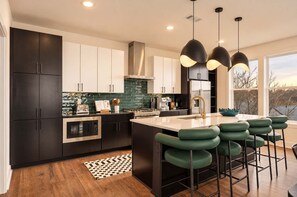 A modern kitchen with dark cabinetry, a central island with bar stools, and pendant lighting. - 2 Chic Nashville Homes | Rooftops & Skyline Views (Nashville)