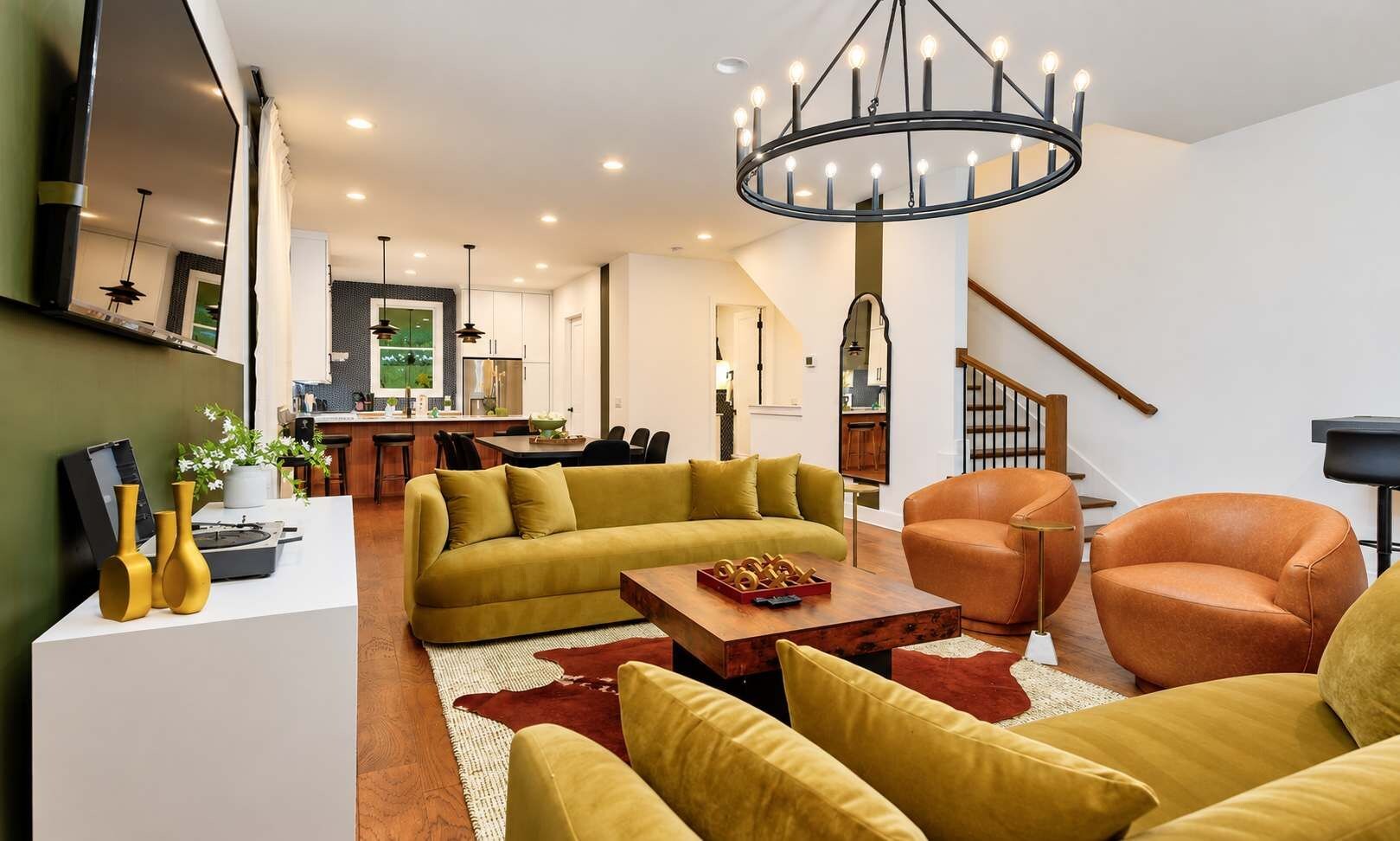 A modern living room with a sofa, armchairs, and a coffee table. A staircase is visible in the background.