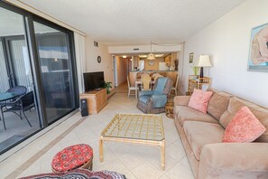 A spacious living area with a sofa, a TV, a dining table, and a kitchen in the background. - Anastasia Condos 614- Steps From the Beach in a 6th Floor Highrise (St. Augustine)