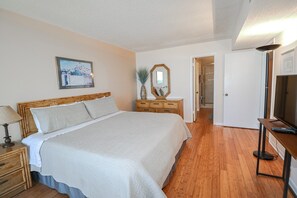 A bedroom with a large bed, bedside tables, a dresser, a mirror, a television, and a door leading to a bathroom. - Anastasia Condos 614- Steps From the Beach in a 6th Floor Highrise (St. Augustine)