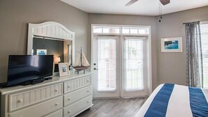 Un dormitorio con cama, cómoda, televisor y ventilador de techo.