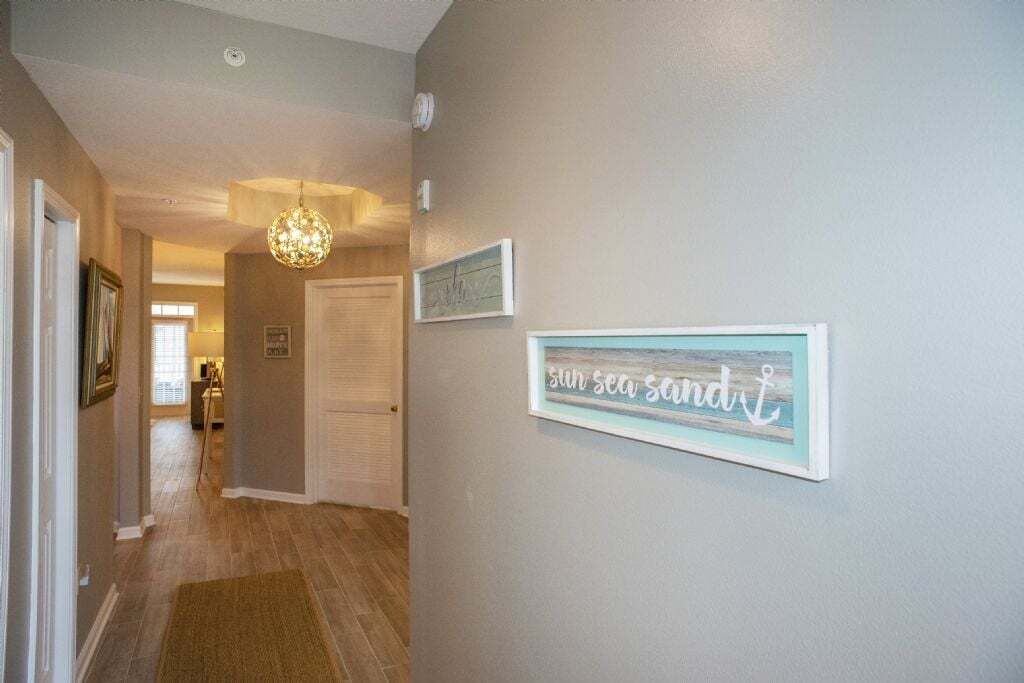 Een hal met een houten vloer, een kroonluchter en een lijst met de tekst 'sun sea sand'.
