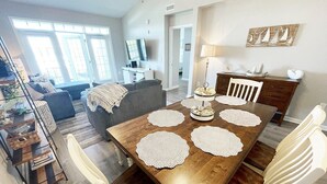 A dining area with a wooden table, white chairs, and decorative placemats. - Seaside at Anastasia G302- Luxury at the Beach! Pool, Wifi, Elevator, Parking (St. Augustine)
