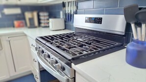 Une cuisine dotée d’une cuisinière en acier inoxydable, de meubles blancs et d’un pare-feu bleu.