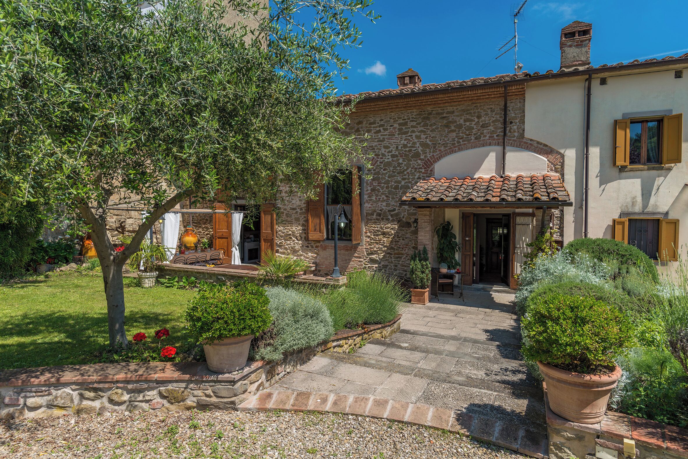 A stone building with a tiled roof, a paved entrance, and potted plants.