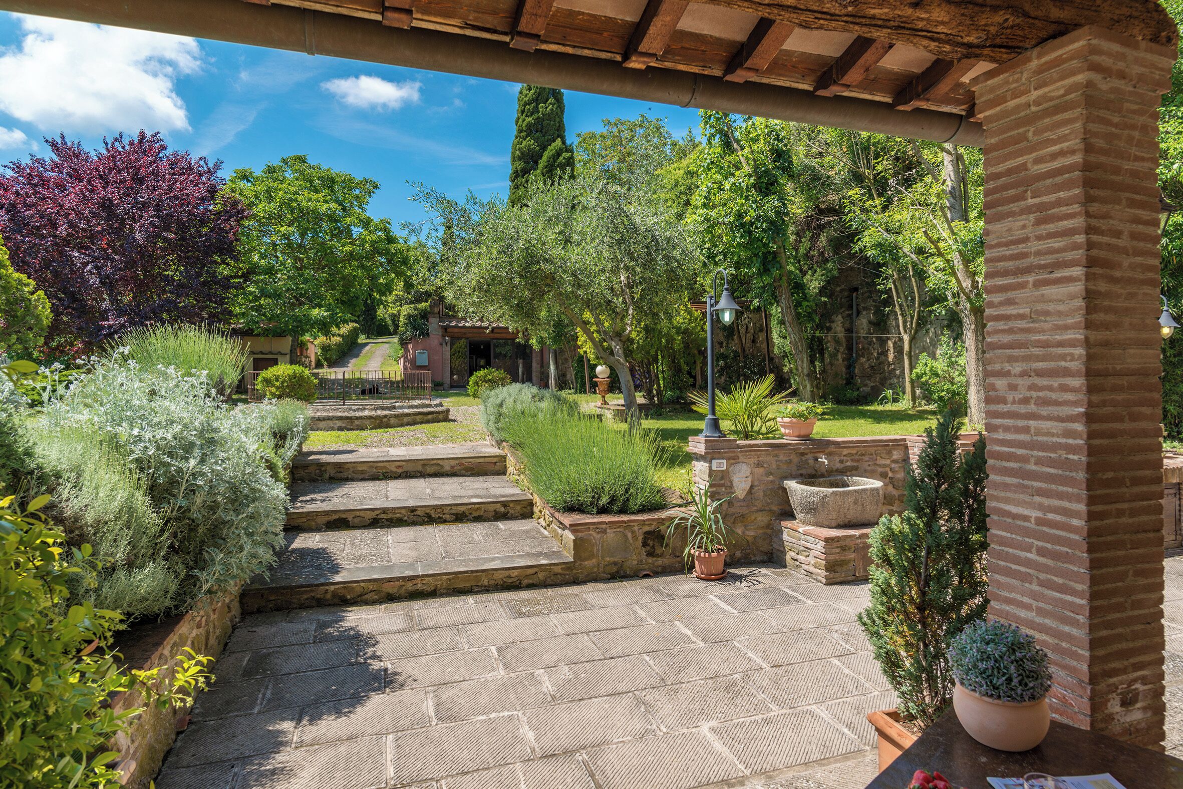 A stone pathway leading to a covered patio area with potted plants and a brick column.