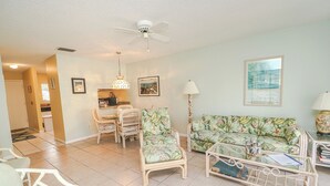 Un salon avec un ventilateur de plafond, un canapé, un fauteuil et une table basse.